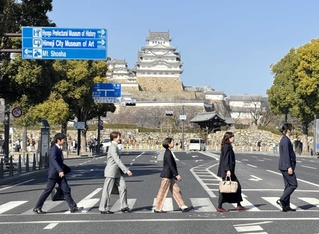 ビートルズのアルバムジャケット「アビーロード」をまねて、姫路城を背景に歩く参加者たち＝姫路市内