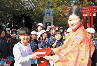 河合寸翁の銅像の前で、集めた修復費を神崎歩宮司（右）に手渡す児童＝姫路市本町、姫路神社