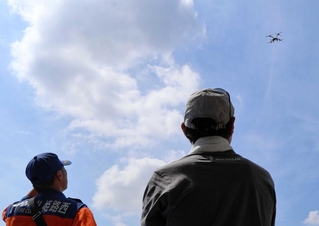 物資搬送のため離陸するドローンを見上げる防災フォーラムの参加者＝青山小学校