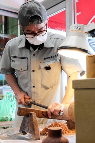工具を使って原木を削り、こまの形にする村岡源水さん＝姫路市東延末３、姫路駅南人形のかきうち