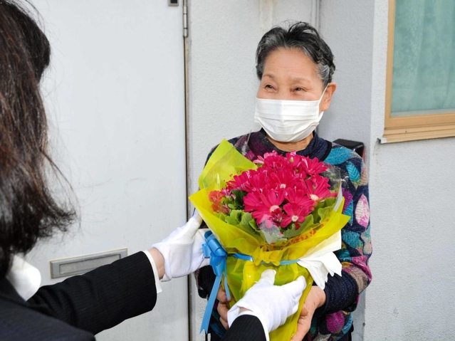 笑顔で花の鉢植えを受け取る高齢者＝西脇市内