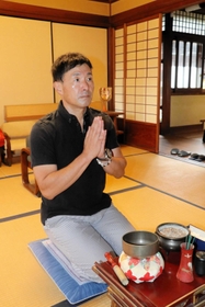 「記事になったことをつゆさんも喜んでいるのでは」。仏壇の前で手を合わせる阿江つゆさんのやしゃご、克彦さん＝加東市