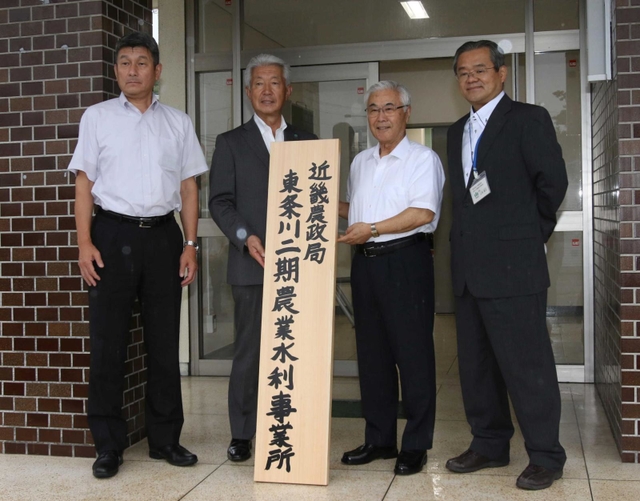 事業所の看板を手にする関係者ら＝加東市社