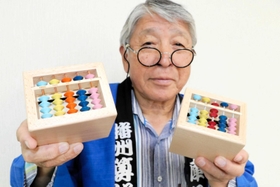 播州算盤工芸品協同組合が開発した賽銭箱型そろばん貯金箱と同組合の宮永英孝理事長＝小野市王子町