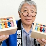 播州算盤工芸品協同組合が開発した賽銭箱型そろばん貯金箱と同組合の宮永英孝理事長＝小野市王子町