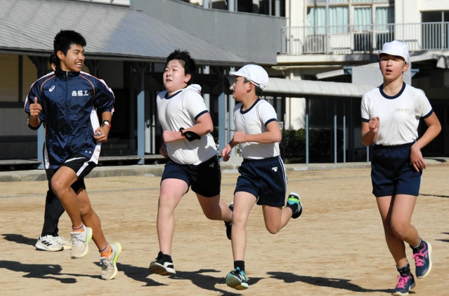 小学生と一緒にグラウンドを駆ける陸上部員＝西脇市西脇