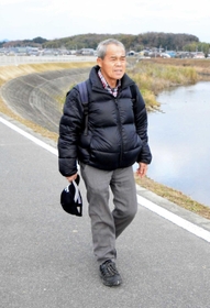 万願寺川沿いを歩く九會田要さん。姿勢を良くするため、背中のリュックサックには砂糖１キロが入っている＝加西市下宮木町