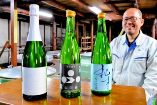 世界的なワイン品評会で入賞した（左から）「祝泡」「特別純米　山田錦」「純青」。奥は稲岡敬之社長＝加西市三口町、富久錦
