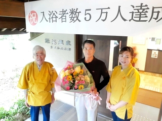 ５万人目となった田中覚さん（中央）に花束などが贈られた＝小野市下来住町、鍬渓温泉きすみのの郷