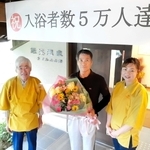 ５万人目となった田中覚さん（中央）に花束などが贈られた＝小野市下来住町、鍬渓温泉きすみのの郷