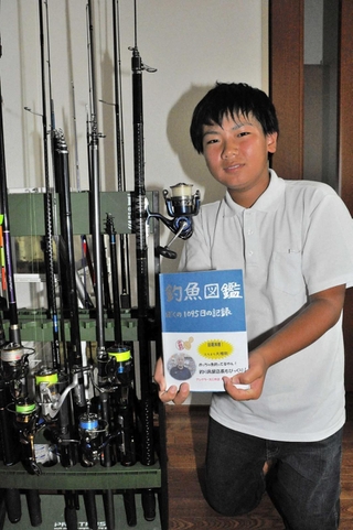 愛用の釣りざおが並ぶそばで「釣魚図鑑」を持つ小西悠貴君＝小野市黒川町