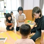こども園の保育士（右）と園児のやり取りを見学する小学校教諭ら（奥）＝西脇市比延町