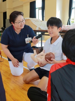 赤ちゃん人形を抱く児童に感想を聞く渋谷純子さん（左）＝丹波篠山市糯ケ坪
