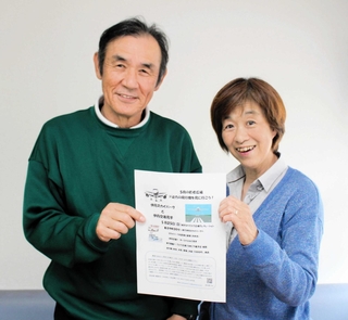 若者広場のチラシを持つ市位辰三さん、葉子さん夫妻＝てとて広場