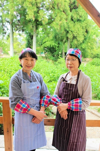 テラス席で新調したエプロンなどを身に着ける柳田みどりさん（右）ら喫茶店の運営メンバー＝ＴＵＭＡこいカフェ