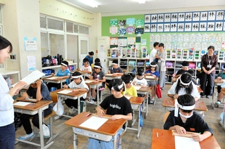 鉢巻き姿でそろばん学習をする４年生。中国の塾代表者らが見守った＝大部小学校