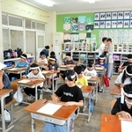 鉢巻き姿でそろばん学習をする４年生。中国の塾代表者らが見守った＝大部小学校