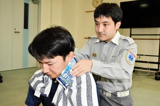 熱中症を和らげるため、首の周りを冷やす方法を助言する光宗研二さん（右）＝加西市北条町西高室、加西消防署