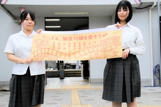 ＪＲ加古川線の中づり広告をデザインした西脇高校の大野愛華さん（左）と笹倉彩愛さん＝西脇市野村町（北播磨県民局提供）