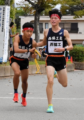 男子・西脇工の６区林恭大選手（右）が、７区岸本周真選手にたすきをつなぐ＝西脇市西脇、市総合市民センター