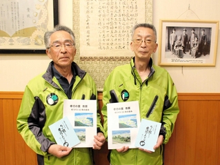 孝行メッセージの冊子や３０年の歩みを手にする池田富美雄さん（右）と中川利彦さん。壁には森安小春さんの写真や賞状などが掲示されている＝市原交流会館
