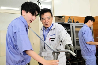 地元の電気工事士（中央）から、配線を通す金属管を曲げる作業を学ぶ生徒＝西脇市野村町