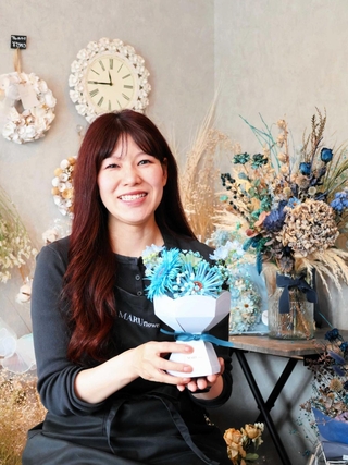 店のコンセプトカラーであるブルーの花を持つ芳原真弥さん＝加東市上滝野