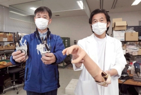 開発した筋電義手を手にする兵庫県立福祉のまちづくり研究所の陳隆明医師（右）と本田雄一郎工学博士＝神戸市西区曙町、同研究所