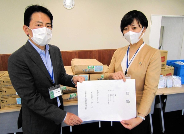 神戸市兵庫区役所の小林隆一郎区長（左）に食料品提供の目録を手渡すコープこうべの担当者＝神戸市兵庫区荒田町１