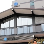 本社機能と３Ｄプリンター工場を備える新社屋を背に、事業展開を語る八十島プロシードの河野浩之専務＝神戸市中央区港島南町３