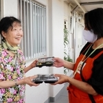 ワタミの宅配弁当と引き換えに空き容器を返却する女性（左）＝神戸市兵庫区菊水町