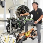 電動三輪ビークル（手前）を開発した石井宏志さん。二輪車エンジニアとして後方にあるバイクの設計にも携わった＝明石市川崎町