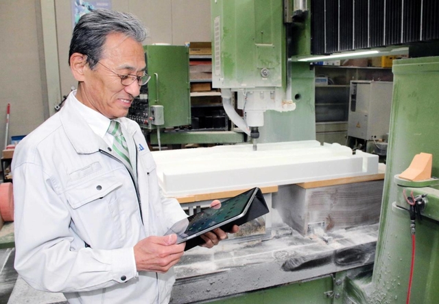 オンライン商談などに使うタブレット端末を手に加工現場に立つイデアの白石泰二社長＝神戸市西区玉津町今津