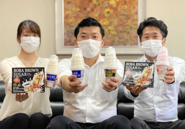 輸出用に生産しているソフトクリームを手にする田口翔一副社長（中央）ら＝田口食品