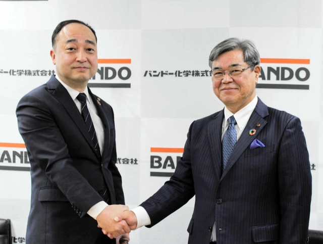 握手を交わす植野富夫氏（左）と吉井満隆氏＝神戸市中央区港島南町４（バンドー化学提供）