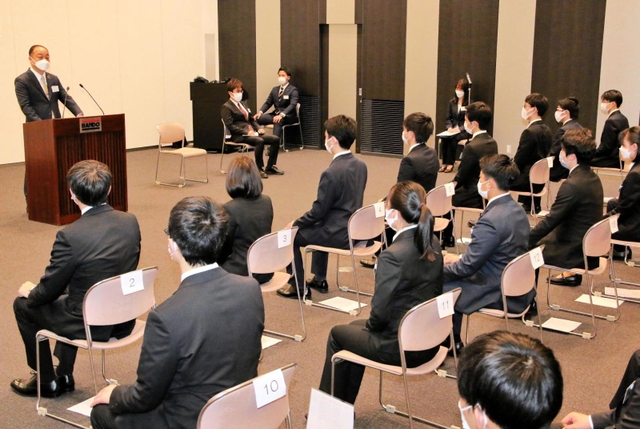 新入社員らに訓示する植野富夫新社長（左奥）＝１日午前、神戸市中央区港島南町４、バンドー化学