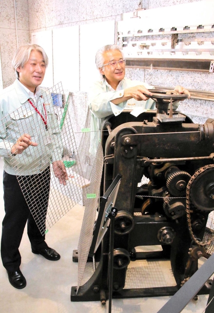 バーベキュー網などに使われる「ガリ線」をつくる機械について説明する奥谷智彦社長（右）＝神戸市中央区相生町４
