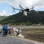 見学者が見守る中、飛行するドローン。右奥に見えるのはロボットトラクター＝姫路市夢前町宮置