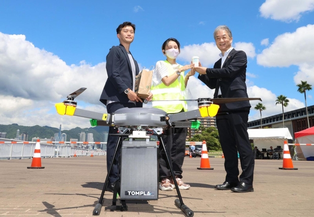 神戸ハーバーランドからドローンによって届けられたスターバックスのアイスコーヒーを受け取る兵庫県産業労働部の竹村英樹部長（右）＝２日午前、神戸市中央区港島１、ポーアイしおさい公園（撮影・長嶺麻子）