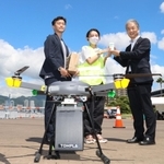 神戸ハーバーランドからドローンによって届けられたスターバックスのアイスコーヒーを受け取る兵庫県産業労働部の竹村英樹部長（右）＝２日午前、神戸市中央区港島１、ポーアイしおさい公園（撮影・長嶺麻子）