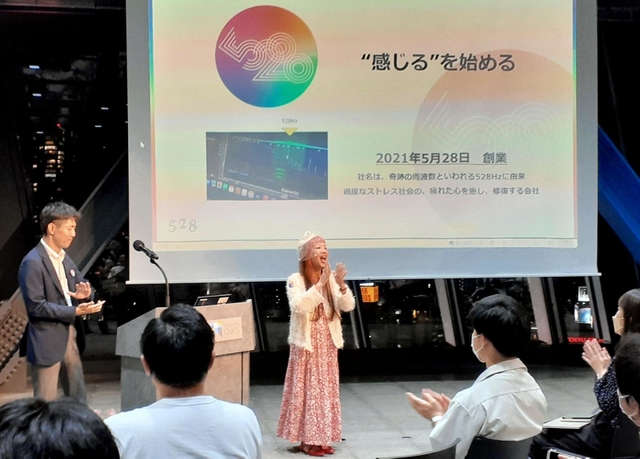 発表の冒頭、歌で観客を引き付けた５２８の玉木浩子代表（中央）＝東京都渋谷区渋谷２