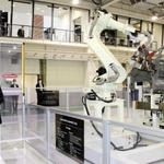 自動車の組み立て用ロボットが並ぶショールームを視察する西村康稔経済産業相（手前）＝１１日午前、神戸市西区櫨谷町松本、川崎重工業西神戸工場