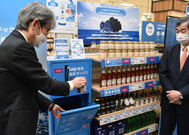 専用容器の返却を実演する兵庫県の服部洋平副知事（左）＝伊丹市池尻４