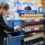 専用容器の返却を実演する兵庫県の服部洋平副知事（左）＝伊丹市池尻４