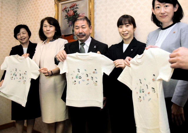 回収した包装紙や間伐材で作ったＴシャツを持つ関係者ら＝神戸市役所