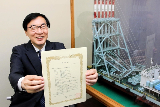 自社の地盤改良船の模型の前で、新工法の評価証を手にする日本海工の山下聖一郎社長＝神戸市中央区伊藤町