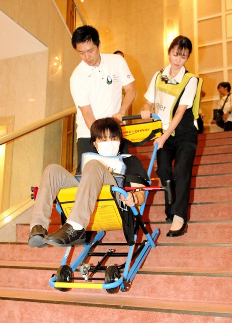 車いす利用者を階段避難車に乗せ、段差を下りる大阪府の吉村洋文知事（左）ら＝大阪府泉佐野市