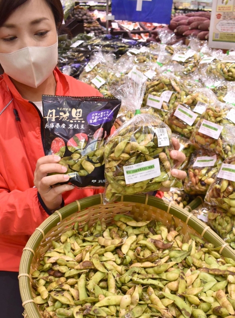 透明の袋に入れた規格外の黒大豆枝豆と通常品を持つコープこうべの吉田智子さん。規格外品はかごに盛り、色や形を紹介した＝神戸市北区日の峰２
