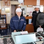 液化水素運搬船「すいそ　ふろんてぃあ」の操舵（そうだ）室で、機器に手を握る菅義偉前首相（中央）＝２５日午後、神戸市中央区神戸空港
