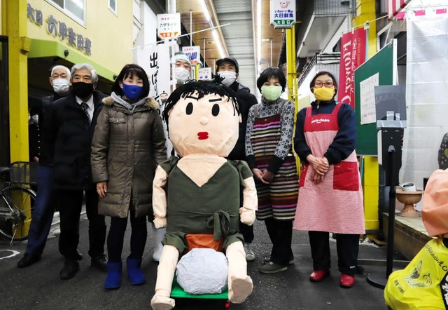 「みのる坊」人形を囲んで笑顔をみせる大日六商店街の店主ら＝神戸市中央区大日通６
